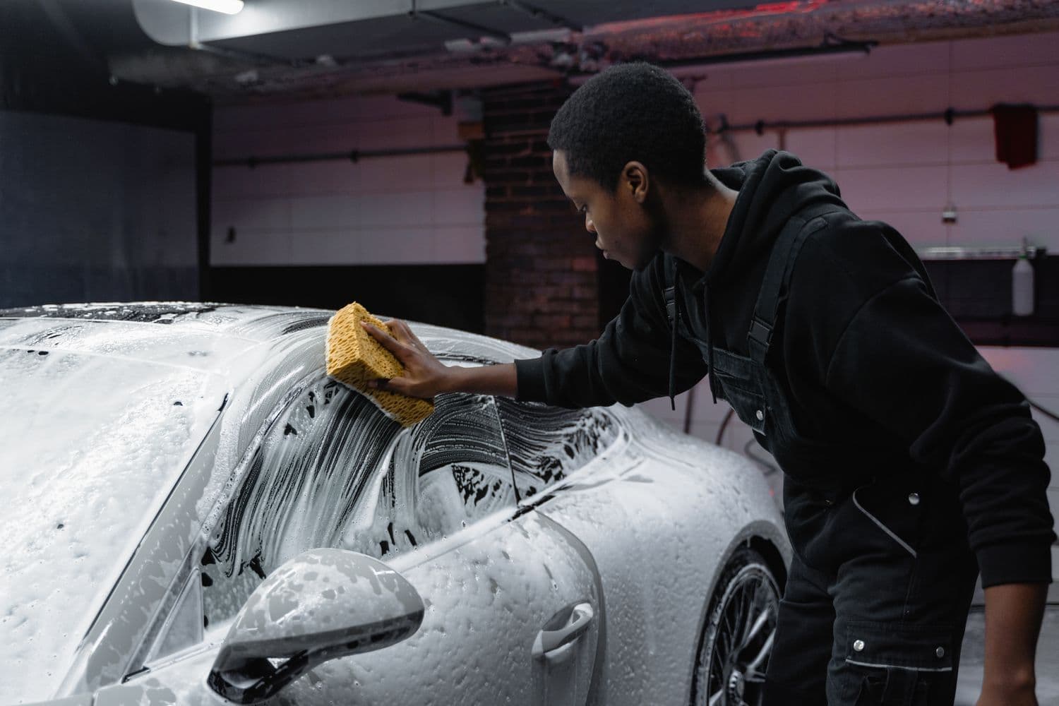 A detailer hand-washing a car in thick foam